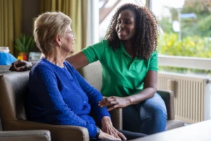 A smiling caregiver talks with an elderly woman in a cozy living room, providing emotional support and companionship as part of home care services.