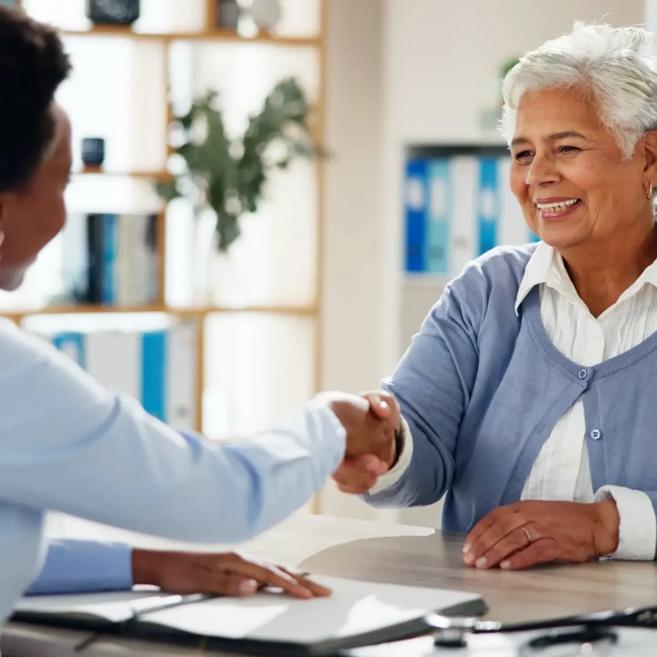 Elderly woman shaking hands with a caregiver after discussing a home care service agreement.