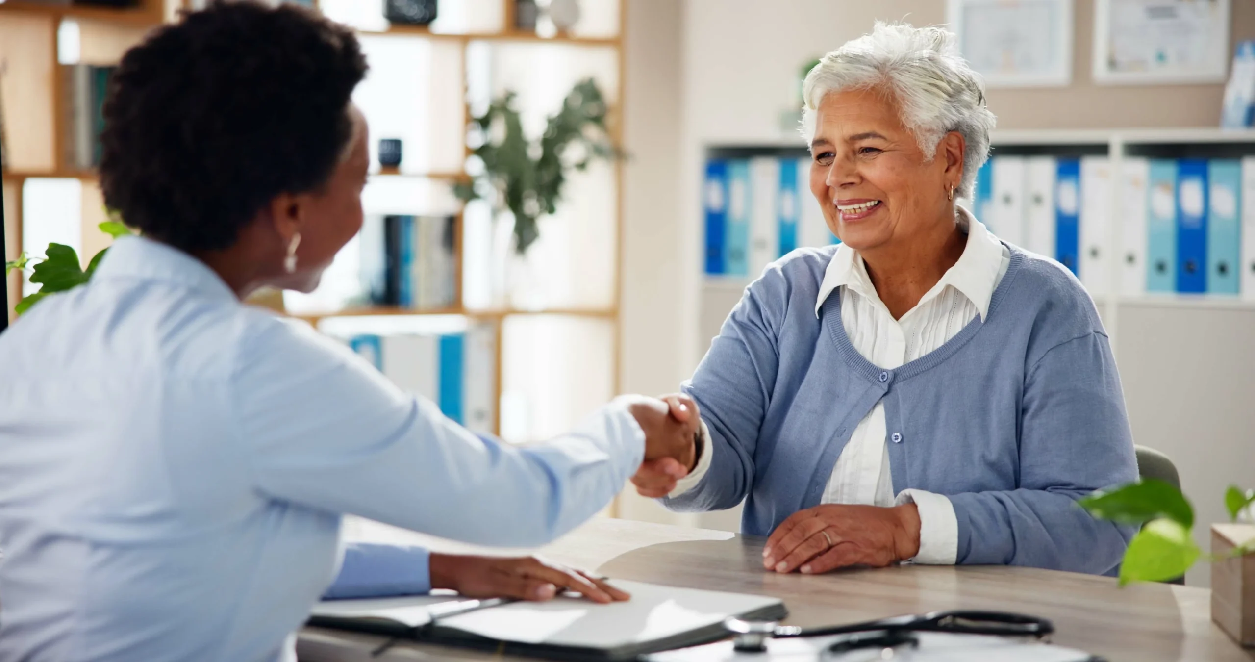 Elderly woman shaking hands with a caregiver after discussing a home care service agreement.