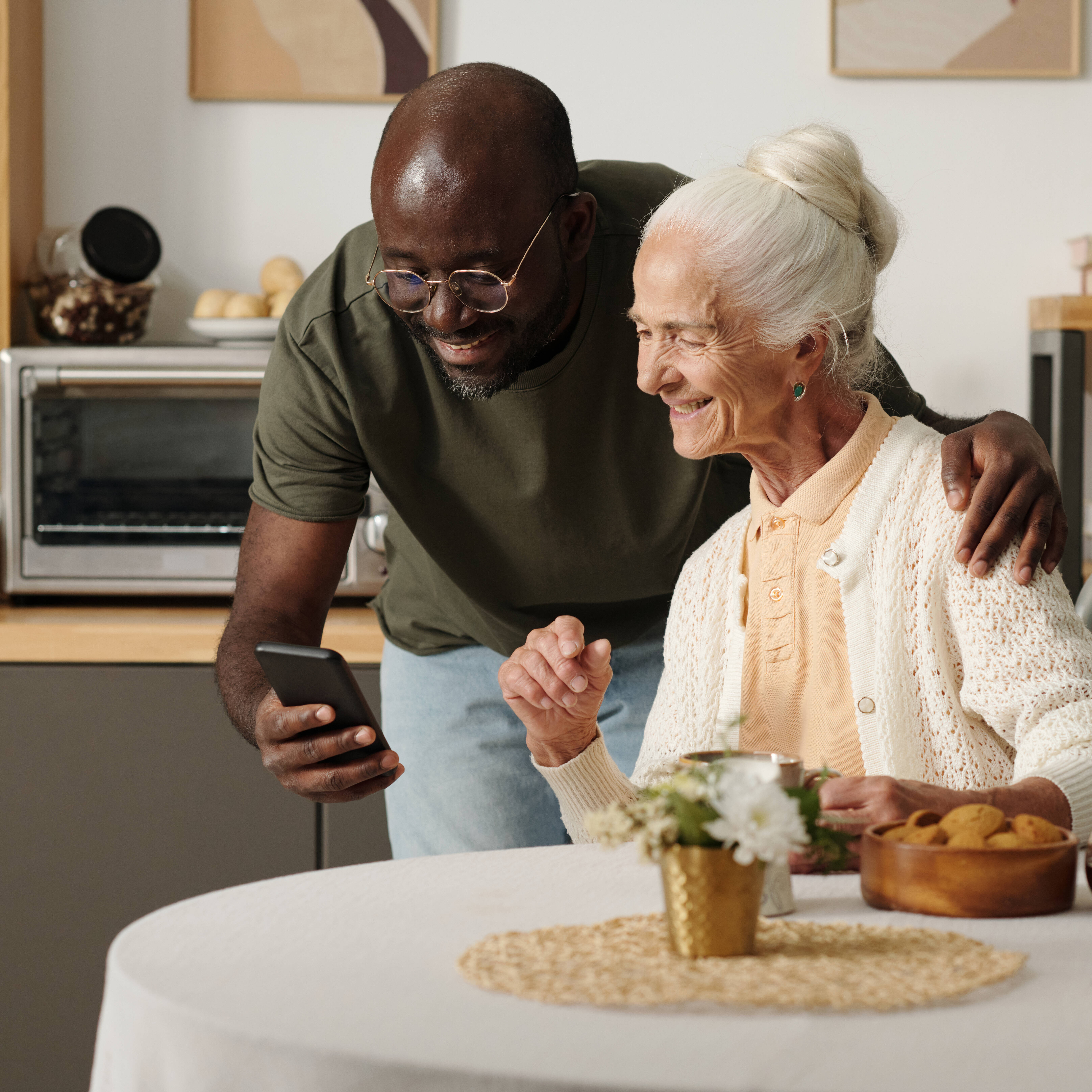Young man teaching elderly woman to use smartphone at home