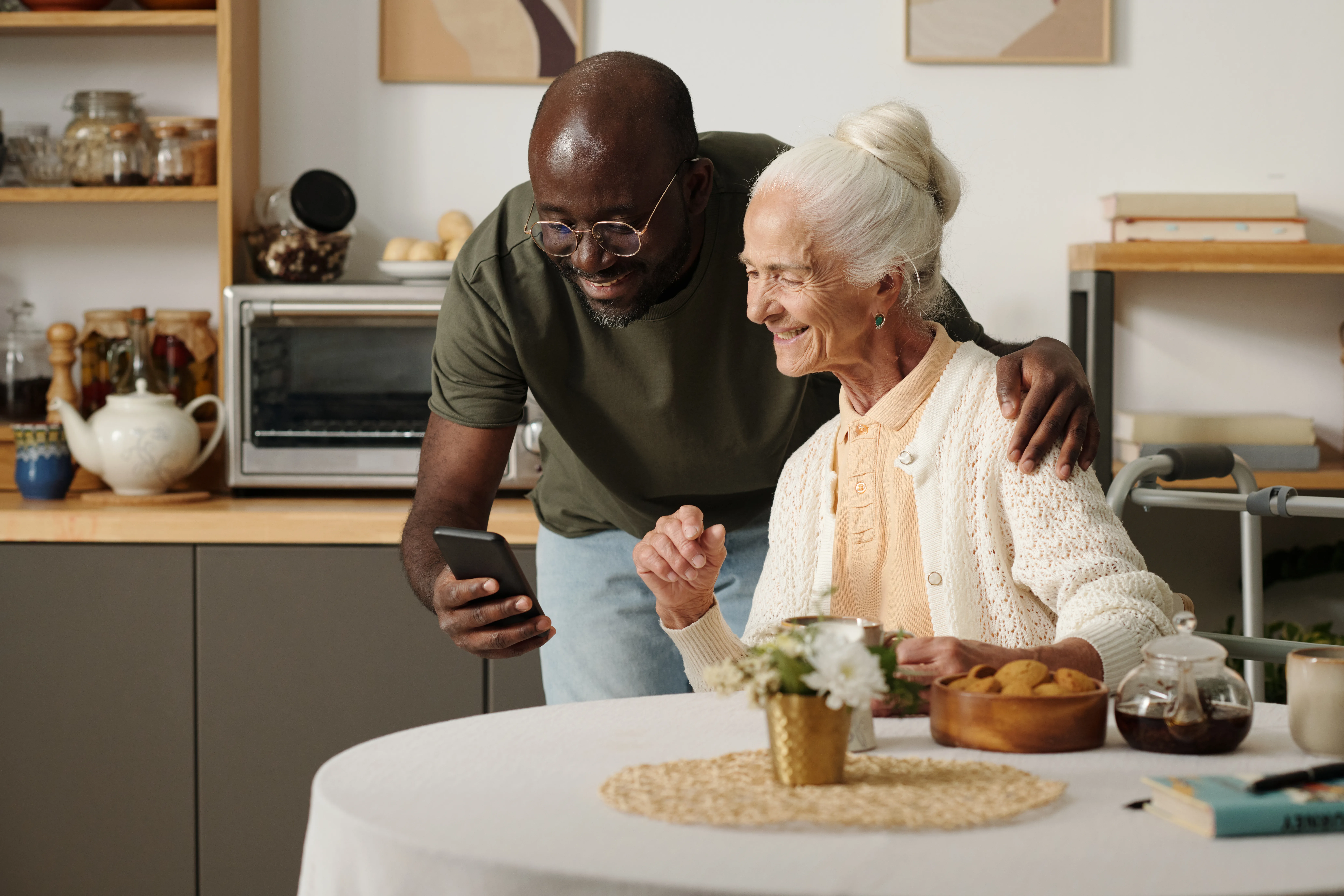 Young man teaching elderly woman to use smartphone at home