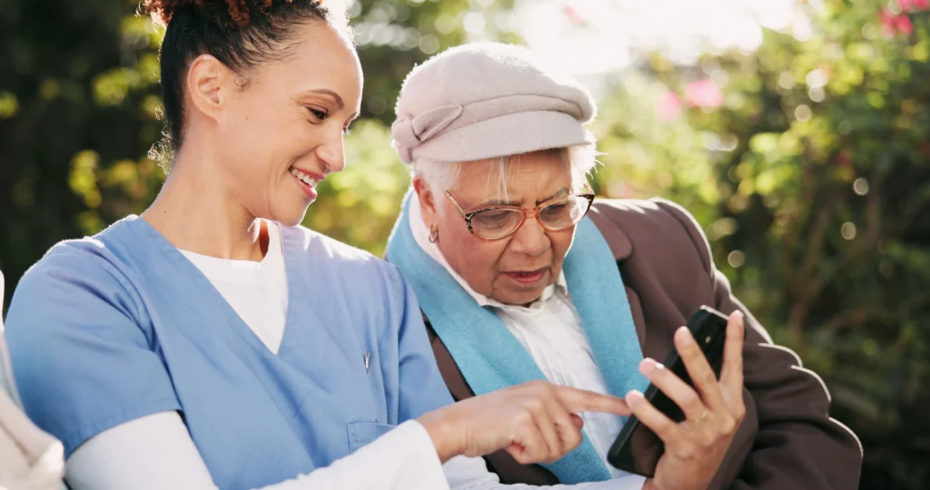 Senior woman learning to use smartphone with caregiver support outdoors