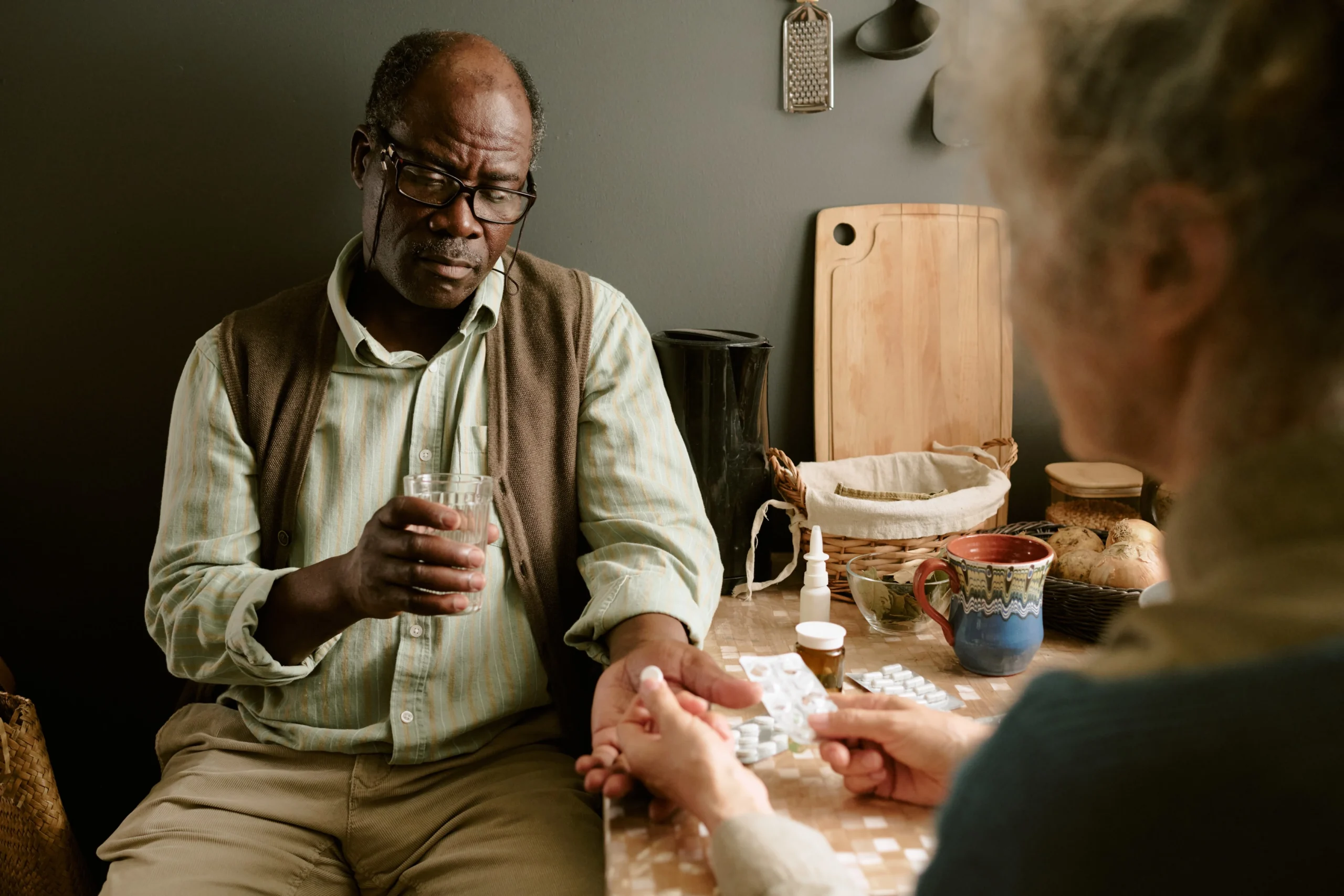 Elderly man with Alzheimer’s receiving medication support from caregiver at home.