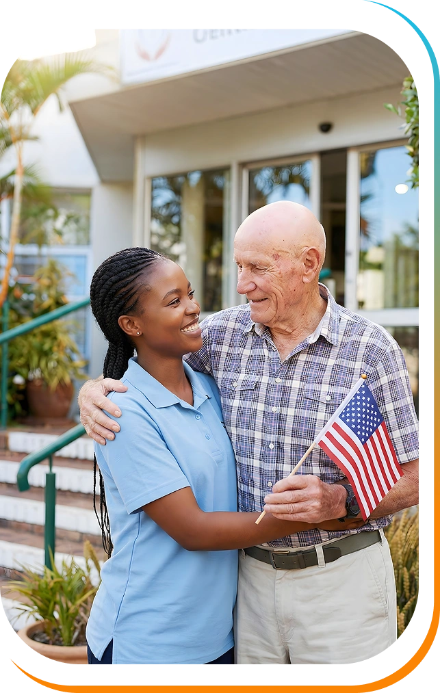 A young woman smiles warmly at an elderly man holding a small American flag. They are standing outside a building, exuding a sense of joy and companionship.