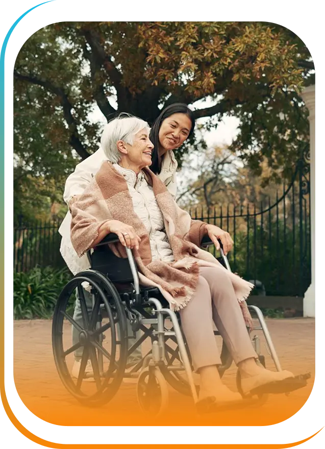 Caregiver pushing an elderly woman in a wheelchair outdoors, sharing a warm moment together.