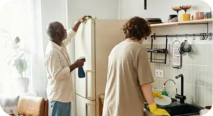Two people cleaning the kitchen together, one wiping the refrigerator and one washing dishes at the sink