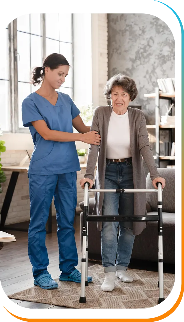 A caregiver in blue scrubs assisting a smiling elderly woman using a walker at home