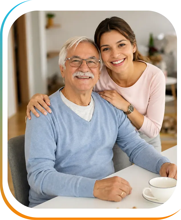 A young woman smiling and embracing an elderly man seated at a table with a coffee cup