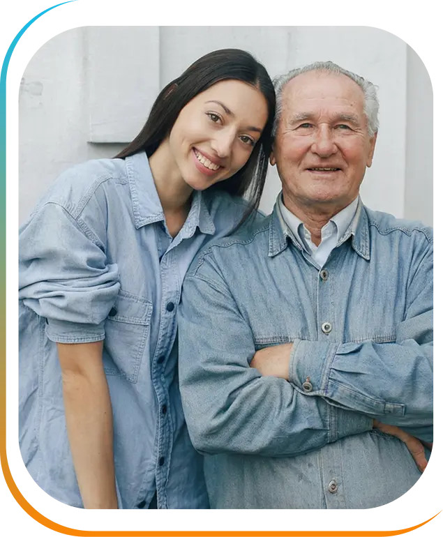 Young woman leaning her head toward a smiling elderly man with crossed arms, both wearing denim shirts